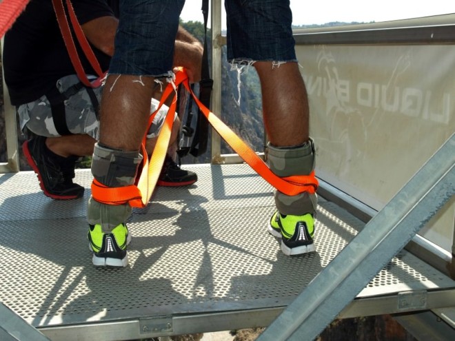 Ο εκπαιδευτής το ελαστικό σχοινί στα πόδια ενός άνδρα που ετοιμάζεται να κάνει bungee jumping από τη γέφυρα της Αράδαινας