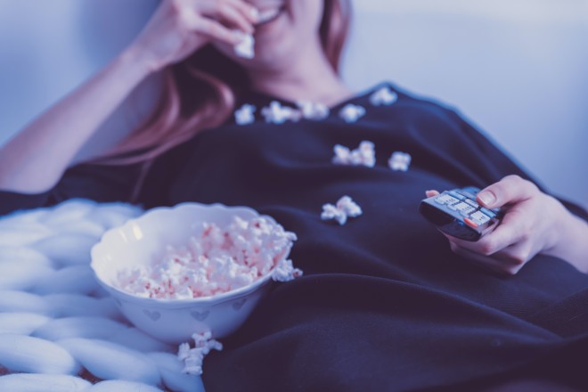 Γυναίκα τρώει ποπ κορν, ενώ παρακολουθεί τηλεόραση ξαπλωμένη στο κρεβάτι