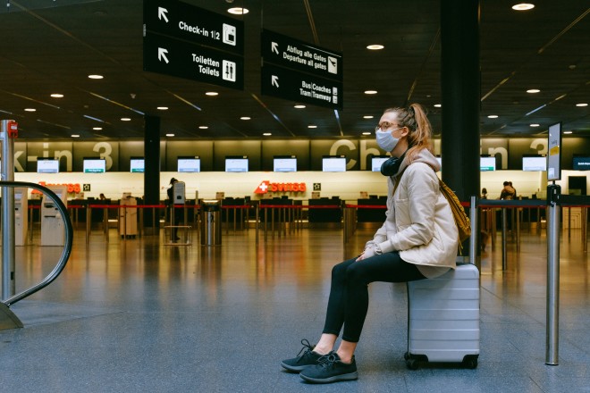 επιβάτης κάθεται στη βαλίτσα της σε αεροδρόμιο, περιμένοντας την πτήση της
