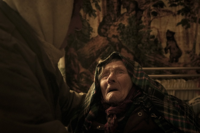 Η Motria Oleksiienko, 99 ετών, τραυματισμένη από τη ρωσική κατοχή, παρηγορείται από τη νύφη Tetiana Oleksiienko σε ένα δωμάτιο χωρίς θέρμανση στο χωριό Andriivka της Ουκρανίας,Τετάρτη, Απριλίου 6, 2022. (AP Photo/Vadim Ghirda)