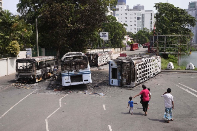 Μια οικογένεια από τη Σρι Λάνκα παρακολουθεί τα συντρίμμια των λεωφορείων που καίγονται μετά από συγκρούσεις στο Κολόμπο της Σρι Λάνκα, Τετάρτη, 11 Μαΐου 2022. (AP Photo/Eranga Jayawardena)