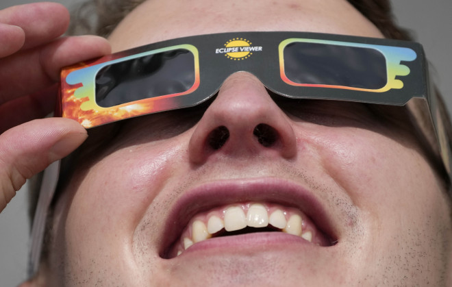 Ένας άνδρας φοράει ειδικά γυαλιά για να παρακολουθήσει τη μερική έκλειψη ηλίου στην πλατεία Τραφάλγκαρ στο Λονδίνο, Πέμπτη 10 Ιουνίου 2021. (AP Photo/Frank Augstein)