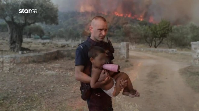 Η φωτογραφία του αστυνομικού Παύλου Τερζόγλου που κουβαλά στην αγκαλιά του ένα παιδί  για να το πάρει μακριά από τις φλόγες στη Νέα Ζωή έγινε πρωτοσέλιδο στον διεθνή Tύπο